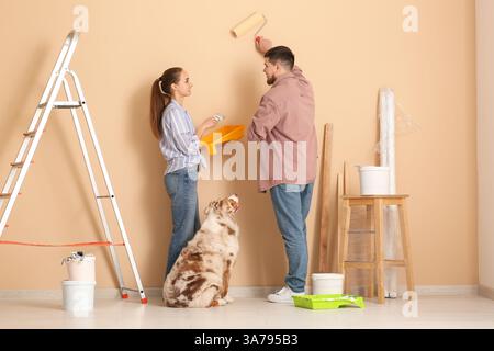 Ein junges Paar mit süßem Hund, der Wände in ihrem neuen Zuhause malt Stockfoto