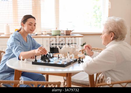Physiotherapeutin mit einer älteren Frau, die Schach am Tisch in der Küche spielt Stockfoto