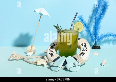 Glas leckerer Cocktail mit Rettungsschirm, Muscheln, Regenschirm und Flipflops auf blauem Hintergrund Stockfoto