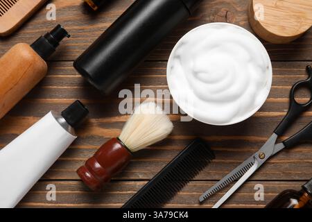 Bürste mit einer Schere, Flaschen mit Kosmetikprodukten und Rasiercreme auf hölzernem Hintergrund Stockfoto