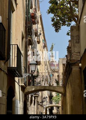 Der Blick entlang der Gasse Carrer de la Carabassa zur Statue unserer Lieben Frau auf der Kuppel der Basilika unserer Lieben Frau von Barmherzigkeit in Barcelona. Stockfoto
