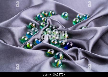 Bunte Glaskugeln auf grauem Stoffhintergrund. Runde grüne Ziersteine. Stockfoto