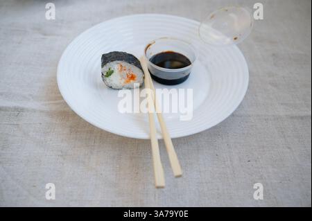Sushi-Rolle mit Stäbchen und Wasabi-Sauce in einem Plastikbehälter auf einer weißen Platte. Stockfoto