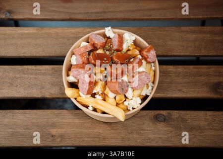 Poutine-Pommes mit Käse und Wurst im Papierbehälter zum Mitnehmen. Köstliche, frisch zubereitete Mahlzeit, perfekt für Menüs, Restaurants oder die Lieferung von Speisen Stockfoto