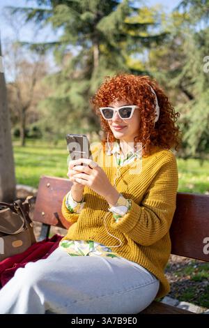 Eine junge Frau genießt fröhlich Musik, während sie sich in einem wunderschönen Park entspannt Stockfoto