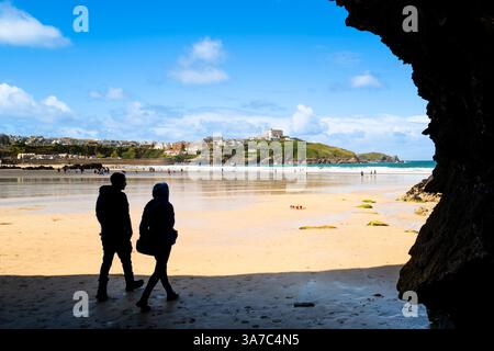 Zwei Personen, die aus einer Höhle an einem sonnigen GT Great Western Beach in Newquay in Cornwall in Großbritannien spazieren. Stockfoto