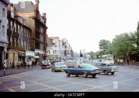 Eine geschäftige Straßenszene in Edinburgh aus den 1970er Jahren fängt die lebhafte Princes Street ein, eine der bekanntesten Straßen der Stadt. Historische Fahrzeuge, Doppeldeckerbusse und Fußgänger füllen die städtische Umgebung mit der Silhouette des Scott Monuments in der Ferne. Fahren Sie von rechts auf die Lothian Road. Stockfoto