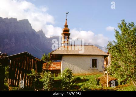 Eine malerische Dorfkapelle in Sixt-Fer-à-Cheval, Haute-Savoie, Frankreich, Juli 1972. Die Kapelle verfügt über eine unverwechselbare Zwiebelkuppel mit einer Wetterfahne, die sich vor den dramatischen Klippen und Berggipfeln der französischen Alpen befindet Stockfoto