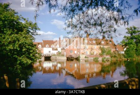 Flatford Mill, eine historische Wassermühle am Fluss Stour in Suffolk, wird hier an einem Sommertag in ruhigem Wasser gezeigt. Die Mühle und die umliegenden Gebäude sind eng mit dem englischen Landschaftsmaler John Constable verbunden, der diese Szene in seinen Werken des frühen 19. Jahrhunderts verewigte. Stockfoto