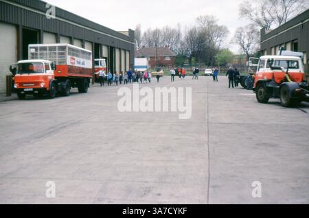 Das Foto aus den 1980er Jahren zeigt eine Gruppe von Kindern und Erwachsenen, die ein Milchlager besuchen, wahrscheinlich im Rahmen eines Schulausflugs oder eines Bildungsbesuchs. Hervorzuheben im Bild sind mehrere rot-weiße Bedford-Lkw der Marke Unigate, die für die Lieferung von Frischmilch verwendet werden. Stockfoto