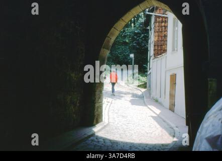 Eine Person läuft durch einen Steinbogen auf einer Kopfsteinpflasterstraße in Hildesheim, Deutschland, August 1990. Stockfoto
