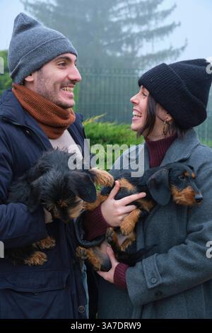 Junge Paare lachen und halten ihre beiden liebenswerten Hunde in einem nebeligen Park während eines kalten Wintertages Navarra SPANIEN Copyright: XMikelxBilbaox/xVWPicsx M-25 Stockfoto