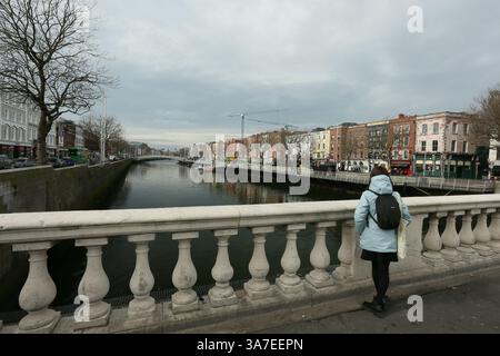 Dublin, Irland - 21. März 2025 - an einem bewölkten, bewölkten Nachmittag hält eine Frau an, um den Liffey von der O'Connell Bridge im Stadtzentrum von Dublin aus zu sehen Stockfoto