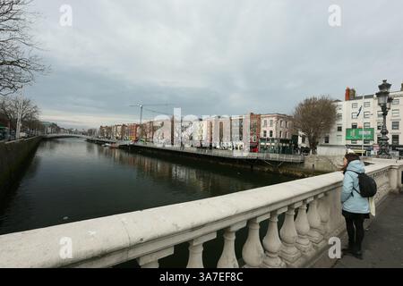 Dublin, Irland - 21. März 2025 - an einem bewölkten, bewölkten Nachmittag hält eine Frau an, um den Liffey von der O'Connell Bridge im Stadtzentrum von Dublin aus zu sehen Stockfoto
