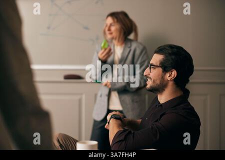 Seitenansicht eines lächelnden jungen Geschäftsmannes mit Brille, der im Besprechungsraum des Büros sitzt Stockfoto