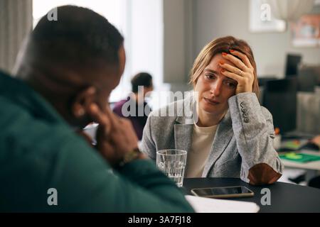 Depressive Geschäftsfrau, die mit einem männlichen Kollegen im Amt spricht Stockfoto
