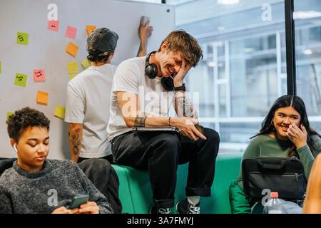 Glücklicher junger Mann, der mit Kopf in Hand auf dem Sofa auf dem College-Campus sitzt Stockfoto