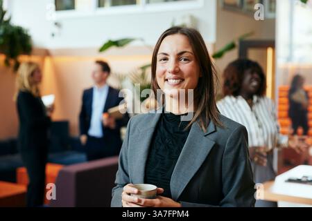 Porträt einer lächelnden jungen Unternehmerin, die einen Tasse in der Lobby hält Stockfoto