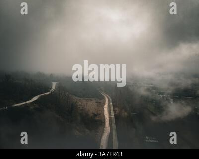Blick auf eine gewundene Bergstraße aus der Vogelperspektive, die in dichten Nebel verschwindet, umgeben von einer natürlichen Landschaft in einer unheimlichen und geheimnisvollen Szene Stockfoto