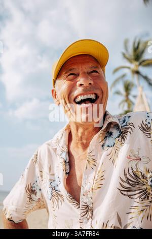 Fröhlicher Seniorenmann mit Mütze und Blick auf den Strand Stockfoto