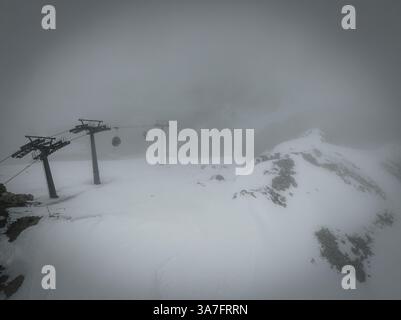 Luftdrohnenaufnahme einer Seilbahn in hoher Höhe, umgeben von schwerem Schnee und dickem Nebel in einer Winterlandschaft Stockfoto