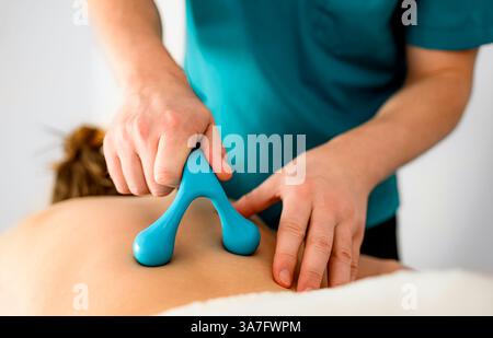 Professioneller Masseur, der eine Rückenmassage mit speziellen Massagezubehör in einem Massagesalon durchführt Stockfoto