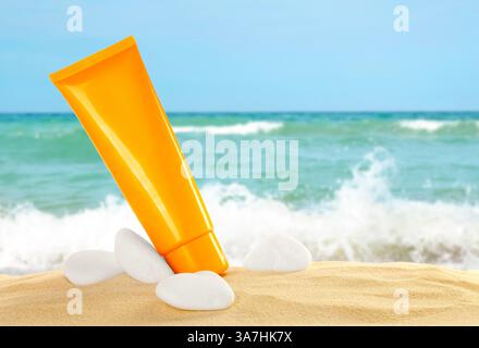 Tube mit Sonnencreme und Stein am Sandstrand in der Nähe des Ozeans Stockfoto
