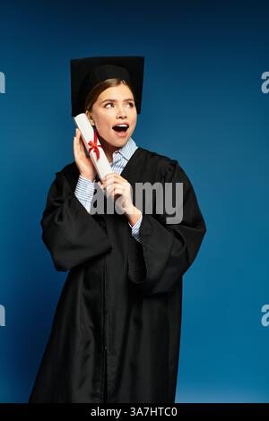 Eine junge Frau hält mit Freude ihr Diplom in ihrem Abschlusskleid und feiert einen Meilenstein. Stockfoto