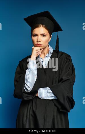Eine junge Frau im Abschlusskleid posiert nachdenklich vor einem auffälligen blauen Hintergrund. Stockfoto