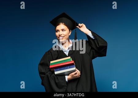 Eine glückliche junge Frau im Abschlusskleid hält bunte Bücher und feiert ihren Erfolg. Stockfoto