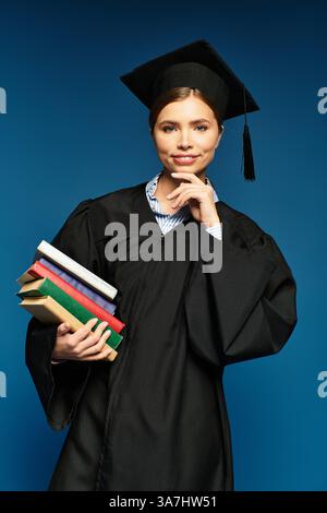 Eine junge Frau in Abschlusskleidung hält Bücher und sieht nachdenklich aus. Stockfoto
