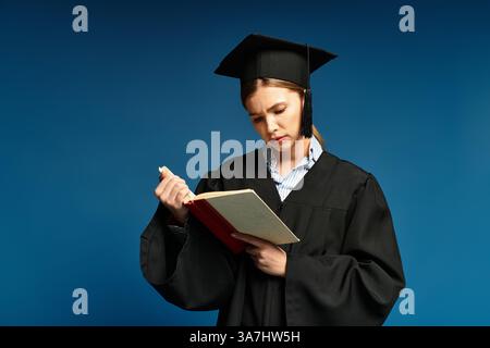 Eine junge Frau im Abschlusskleid, die sich stark auf ein Buch konzentriert, symbolisiert den akademischen Erfolg. Stockfoto