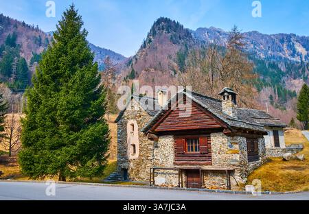 Traditionelle Alpensteinhäuser in den Bergen, bedeckt mit Nadelwäldern, Mogno, Lavizzara, Vallemaggia, Tessin, Schweiz Stockfoto