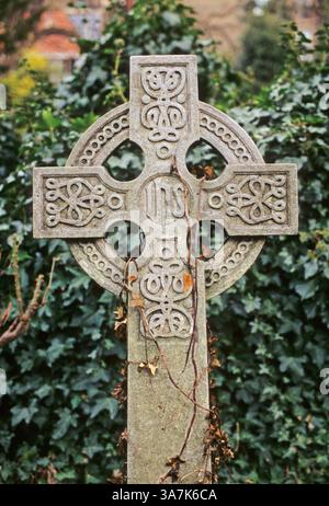 Grabstein in keltischer Form vor einem Hintergrund von Efeublättern auf dem Highgate Cemetery, London, England, Vereinigtes Königreich Stockfoto