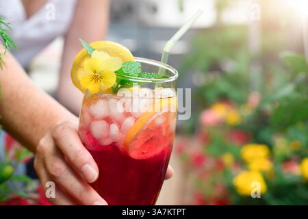 Frau greift mit einem bunten roten, kalten Sommergetränk auf einem Balkon oder einer Terrasse hinein Stockfoto