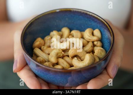 Cashewnüsse. Nahaufnahme von weiblichen Händen, die eine Schüssel voller Cashewnüsse halten. Stockfoto
