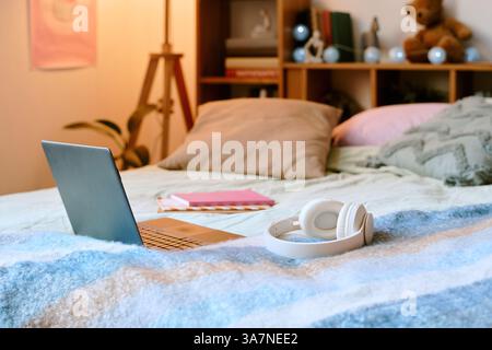 Einladende Schlafzimmerszene mit Laptop, Kopfhörern und Büchern auf dem Bett für einen gemütlichen Arbeitsplatz mit künstlerischen und persönlichen Details Stockfoto
