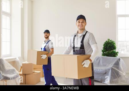 Lächelnde professionelle Umzugswagen, die Kartonschachteln tragen und bei der Standortverlagerung zu Hause helfen. Stockfoto