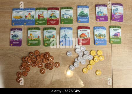 Mozyr, Weißrussland, 10. April 2024: Brettspiel Machi Koro. Vorbereitung auf das Spiel. RaMachi Koros Upgrade- und Münzkarten. Stockfoto