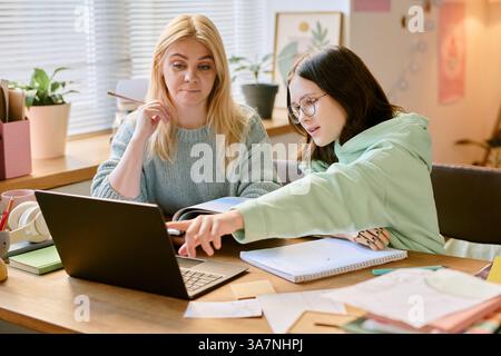 Zwei Frauen tauschen Ideen am Schreibtisch aus, während sie an einem Laptop arbeiten und Notizen machen, intellektuelle Diskussionen führen und eine kreative und kollaborative Atmosphäre genießen Stockfoto