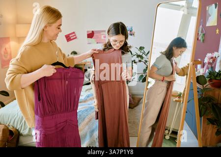 Mutter und Tochter untersuchen Kleider im Schlafzimmer Spiegelreflexlicht, einer hält ein rosa Kleid, während der andere das Spiegelbild betrachtet Stockfoto