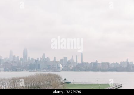 Weiche Wolken bedecken die Skyline von New York, während die Menschen am frühen Morgen entlang des Ufers von New Jersey spazieren. Stockfoto