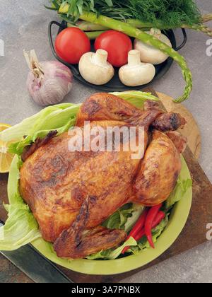 Ein perfekt geröstetes Huhn sitzt auf einem Bett aus knusprigem Salat, umgeben von lebendigem Gemüse und einer Zitrone, bereit für einen Familientreffen. Stockfoto