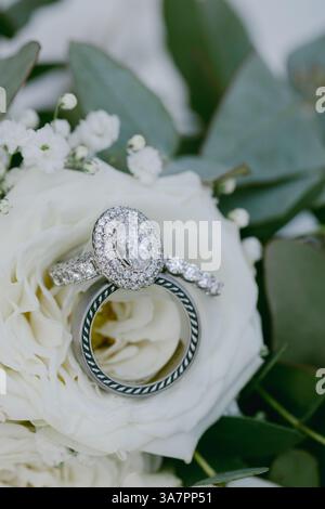 Elegante Eheringe aus Diamant und Silber liegen auf einer weißen Blume und betonen komplexe Details in einer romantischen Umgebung. Stockfoto