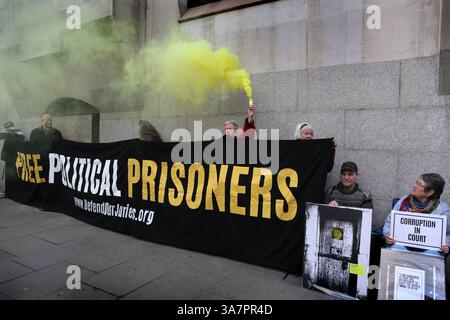 London, England, Großbritannien. März 2025. Anhänger der Verteidigung unsere Jurys sitzen mit gelben Rauchfackeln und einem Banner mit der Aufschrift˜Freie politische Gefangene“ während des Protestes vor dem Old Bailey. Freunde und Familie versammeln sich vor dem Old Bailey in London, um Lärm zu machen und den Aktivisten der Filton 18 Palestine Action, die im Gefängnis festgehalten wurden, zu unterstützen, nachdem sie im August 2024 im Rahmen des Terrorismusgesetzes verhaftet worden waren, nachdem sie in die Elbit Systems-Anlage in Filton, Bristol, eindrangen, wo sie einen Schaden von über Â Million Pfund verursachten und die Fabrik zum Stillstand brachten. Stockfoto
