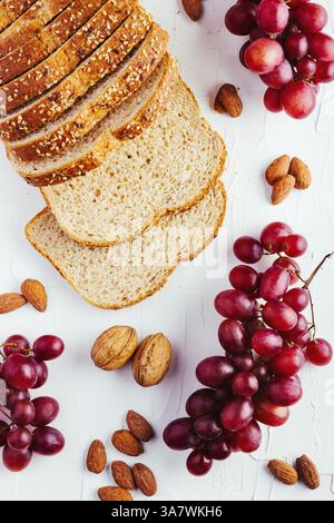 Draufsicht Komposition mit Brotscheiben und rot und grün Trauben auf weißem Tisch mit Walnüssen und Mandeln angeordnet Stockfoto