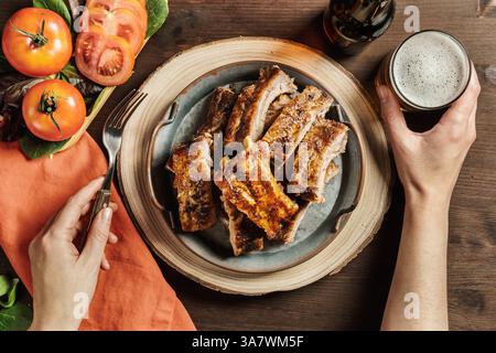 Von oben der Ernte anonyme Person sitzt am Tisch in Cafe mit leckeren Grillfleisch Rippchen und ein Glas Bier Stockfoto