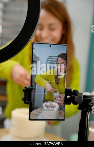hispanische Frau filmt sich mit ihrem Handy, während sie einen Kuchen zubereitet Stockfoto