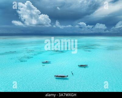 Blick aus der Vogelperspektive auf farbenfrohe Boote und Yachten in klarem Wasser im Sommer. Insel Mnemba, Sansibar. Blick von oben auf Sandbank bei Ebbe, blaues Meer, schwimmende Menschen Stockfoto