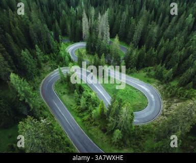 Blick aus der Vogelperspektive auf die kurvige Bergstraße und den grünen Wald im Sommer. Dolomiten, Italien. Blick von oben auf die gewundene Straße am Bergpass, Bäume im Frühling. Schlange RO Stockfoto